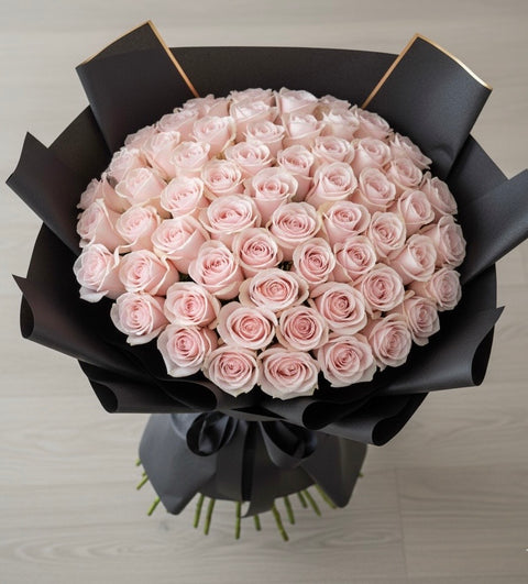Bouquet of pink roses wrapped in black paper on a light gray background