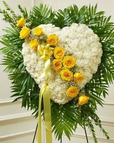 This solid heart standing spray, accented with a slash of beautiful yellow roses, is a loving symbol of your sympathy and support. White carnations, yellow roses, baby's breath and more make up this solid heart with oasis in mache, tied to the wire easel with satin ribbon. Traditionally sent directly to the funeral home by family members or friends and displayed on a stand.