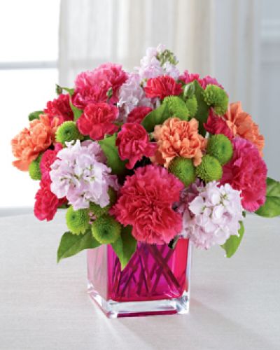 <p>Dazzling and delightful, this bold and colorful flower bouquet is set to impress with it's high impact look and graceful styling. Hot pink carnations, orange carnations, pale pink gilly flower, hot pink mini carnations, green button poms, and lush greens are beautifully arranged in a raspberry pink glass cubed vase to create a rush of fun and warm wishes to send straight to your recipient's door.</p>