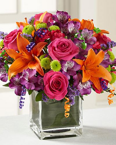 Birthday blooms that are ready to get your recipient's special day started, this flower bouquet is bright, happy, and ready to celebrate! Hot pink roses and orange Asiatic Lilies are vibrant and fun surrounded by purple Peruvian Lilies, hot pink mini carnations, green button poms, purple statice, and an assortment of lush greens. Accented with assorted curling ribbons to give it that party feels and presented in a clear glass cubed vase lined with ti leaf green material for added beauty, this unforgettable birthday bouquet is that ultimate surprise that will make them feel the love on their big day.

STANDARD bouquet includes 11 stems.
Approximately 10H x 10W.
C Quantity Color Description
2 Hot Pink 50 cm Standard Rose
1 Orange Asiatic Lily
3 Purple Alstroemeria
2 Green Button Pom
2 Hot Pink Miniature Carnation
1 Purple Filler - Sinuata Statice
2 Green Green - Leather Leaf
1 Green Green - Pittosporum
0.33 Green Green Flexible Leaf Material
1.5 Curling Ribbon (yds.)
0.33 Green Florist Foam Brick

DELUXE bouquet includes 15 stems.
Approximately 11H x 11W.
C Quantity Color Description
4 Hot Pink 50 cm Standard Rose
1 Orange Asiatic Lily
3 Purple Alstroemeria
2 Green Button Pom
3 Hot Pink Miniature Carnation
2 Purple Filler - Sinuata Statice
2 Green Green - Leather Leaf
1 Green Green - Pittosporum
0.33 Green Green Flexible Leaf Material
1.5 Curling Ribbon (yds.)
0.33 Green Florist Foam Brick

PREMIUM bouquet includes 19 stems.
Approximately 12H x 12W.
C Quantity Color Description
5 Hot Pink 50 cm Standard Rose
2 Orange Asiatic Lily
4 Purple Alstroemeria
3 Green Button Pom
3 Hot Pink Miniature Carnation
2 Purple Filler - Sinuata Statice
2 Green Green - Leather Leaf
1 Green Green - Pittosporum
0.66 Green Green Flexible Leaf Material
3 Curling Ribbon (yds.)
0.5 Green Florist Foam Brick